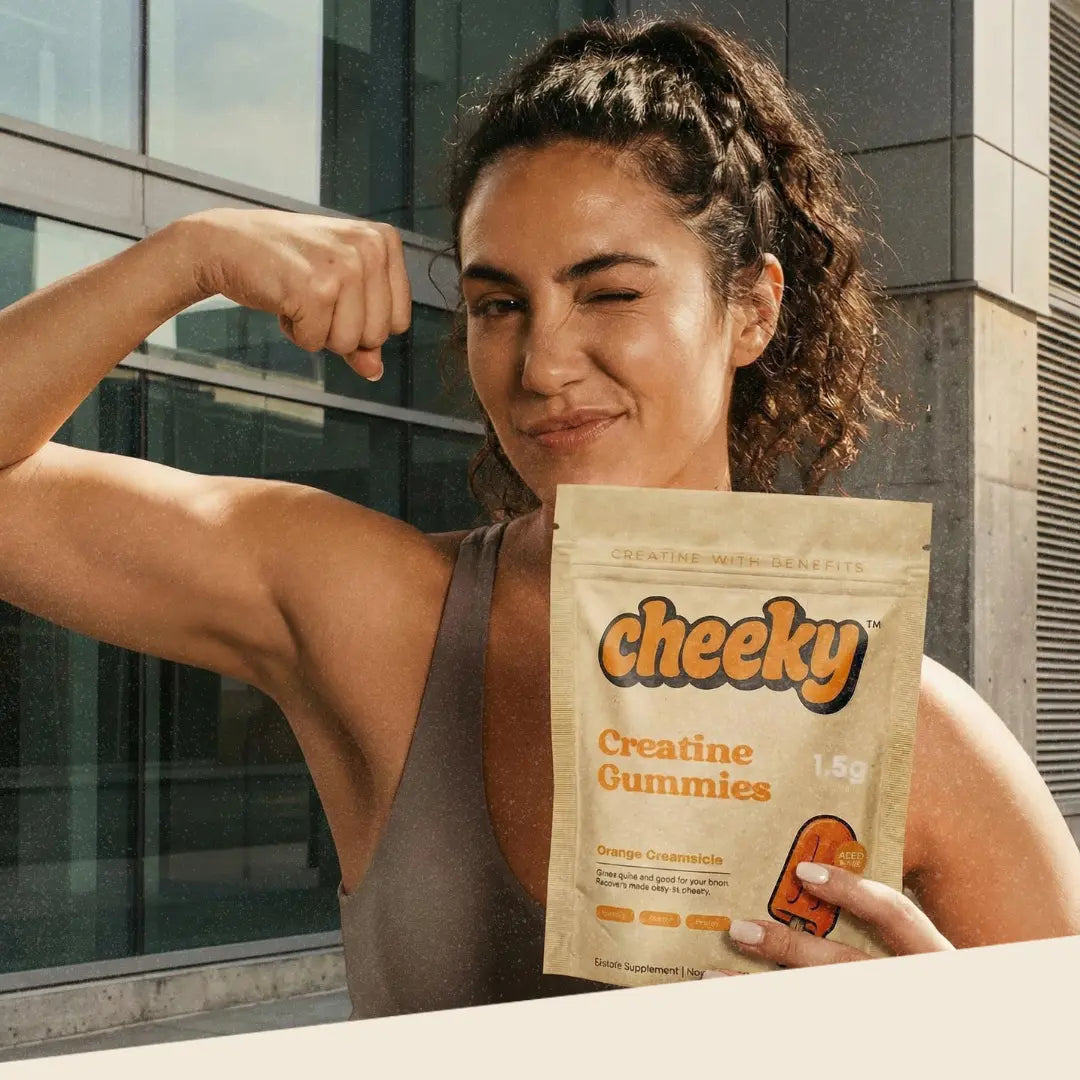 Woman holding Cheeky creatine gummies while flexing arm, orange creamsicle flavor